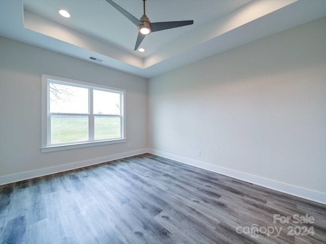 spare room with a raised ceiling, ceiling fan, and dark wood-type flooring