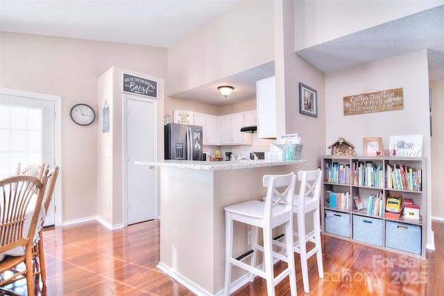 3076 Champion Ln SW, Concord, NC 28025 - kitchen featuring stainless steel fridge with ice dispenser, light wood-style floors, white cabinets, a kitchen breakfast bar, and a peninsula