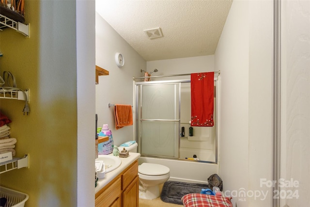 full bathroom featuring toilet, vanity, a textured ceiling, and combined bath / shower with glass door