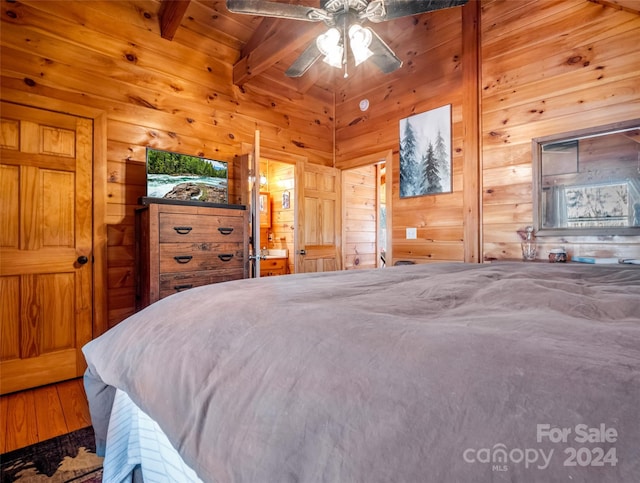 bedroom with vaulted ceiling with beams, ceiling fan, wood walls, and hardwood / wood-style flooring