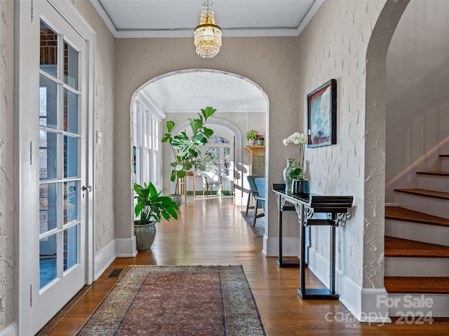 foyer with crown molding, wood-type flooring, and a notable chandelier