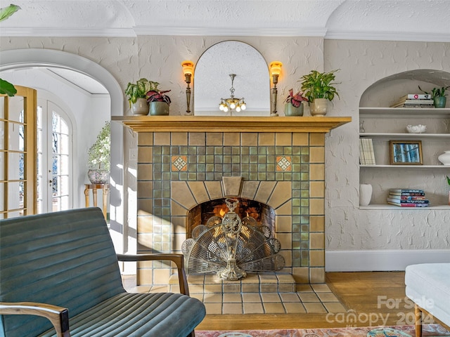 interior space with a tile fireplace, crown molding, a textured ceiling, and hardwood / wood-style flooring