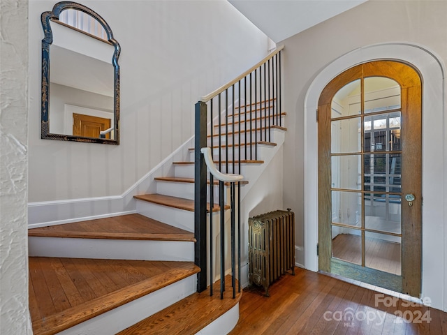 stairs with hardwood / wood-style floors and radiator heating unit