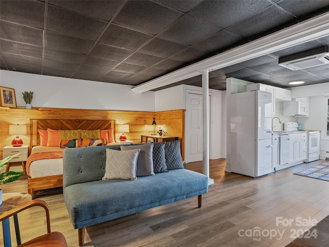 bedroom featuring hardwood / wood-style flooring, white fridge, and wooden walls