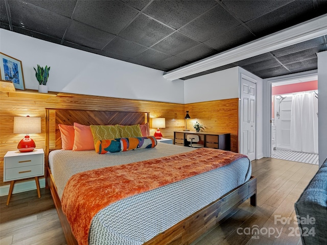 bedroom featuring wood walls, a drop ceiling, and wood-type flooring