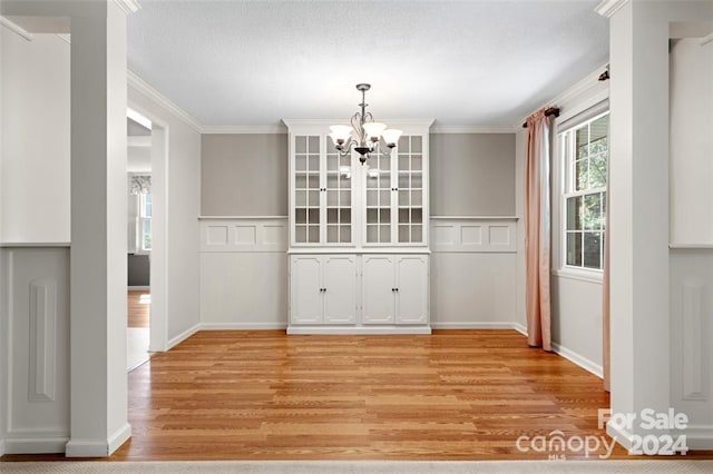 unfurnished dining area featuring light wood-type flooring, ornamental molding, and a notable chandelier