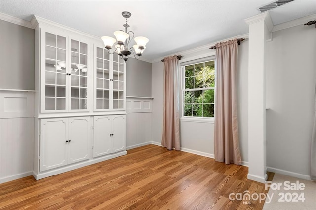 unfurnished dining area featuring a chandelier, light wood-type flooring, and ornamental molding