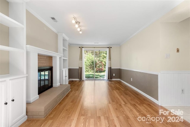 unfurnished living room featuring built in features, ornamental molding, light hardwood / wood-style flooring, and a brick fireplace