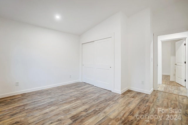 unfurnished bedroom featuring a closet, light hardwood / wood-style floors, and vaulted ceiling