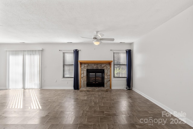 unfurnished living room featuring a stone fireplace, plenty of natural light, and ceiling fan