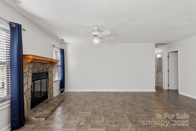 unfurnished living room featuring a textured ceiling, a stone fireplace, and ceiling fan