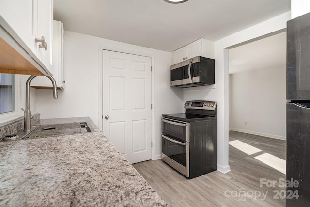 kitchen with white cabinetry, sink, light stone counters, light hardwood / wood-style flooring, and appliances with stainless steel finishes