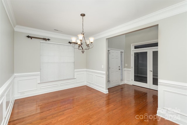 empty room with french doors, an inviting chandelier, ornamental molding, and hardwood / wood-style floors