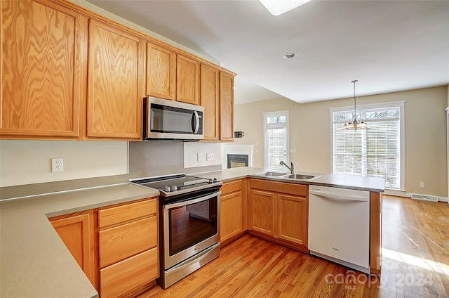 kitchen featuring sink, hanging light fixtures, stainless steel appliances, a notable chandelier, and light wood-type flooring