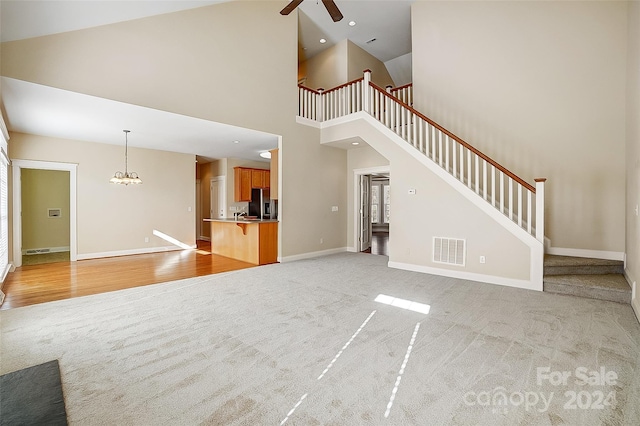 unfurnished living room with ceiling fan, a towering ceiling, and light carpet