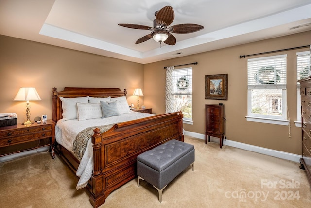 bedroom with ceiling fan, light carpet, a tray ceiling, and multiple windows