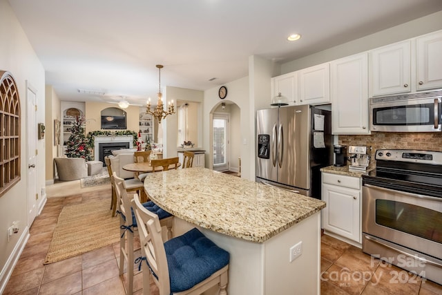 kitchen with white cabinets, decorative light fixtures, light stone counters, and appliances with stainless steel finishes