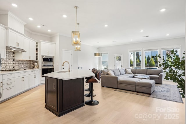 kitchen featuring appliances with stainless steel finishes, backsplash, a kitchen island with sink, sink, and white cabinets