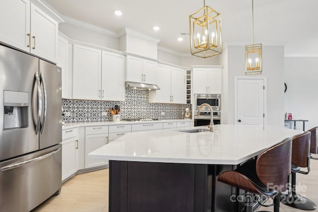 kitchen with white cabinetry, crown molding, decorative light fixtures, a kitchen island with sink, and appliances with stainless steel finishes