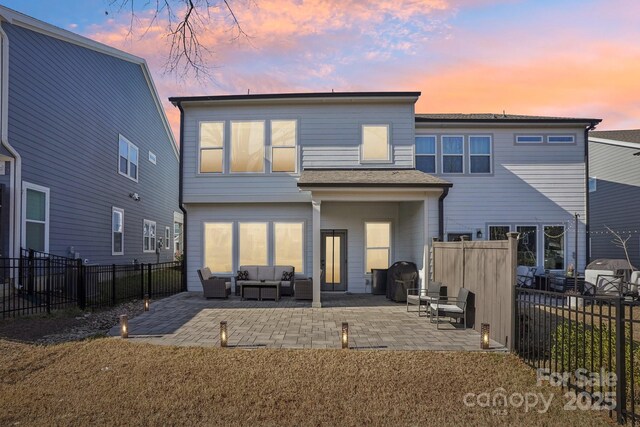 back house at dusk with outdoor lounge area and a patio