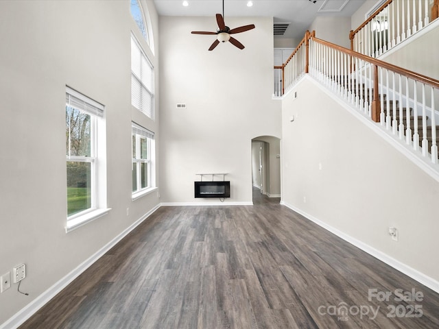 unfurnished living room featuring ceiling fan, dark hardwood / wood-style flooring, and a towering ceiling