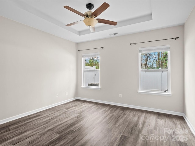 spare room with dark wood-type flooring, a raised ceiling, and ceiling fan