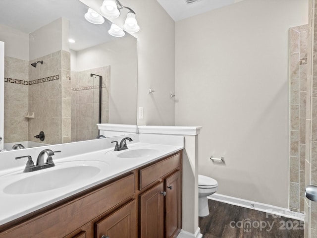 bathroom with tiled shower, toilet, vanity, and wood-type flooring