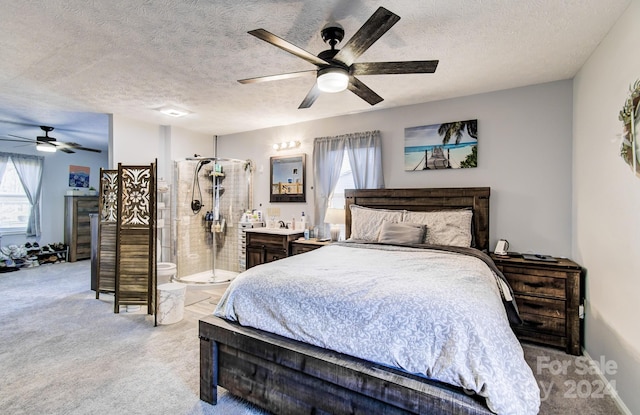 bedroom with ceiling fan, light colored carpet, a textured ceiling, and connected bathroom