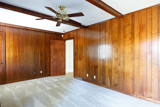 carpeted empty room with beamed ceiling, ceiling fan, and wooden walls