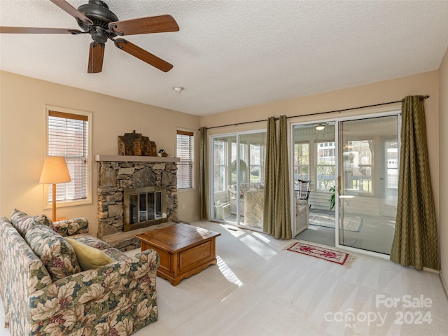 living room with ceiling fan, a stone fireplace, light colored carpet, and a textured ceiling