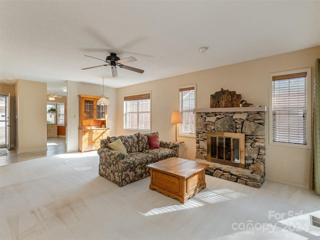 carpeted living room with a stone fireplace, ceiling fan, and a textured ceiling