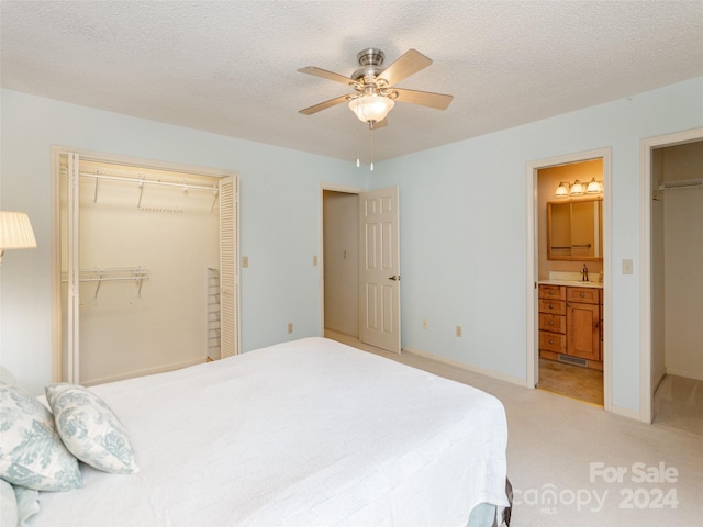 bedroom featuring ensuite bathroom, ceiling fan, light carpet, and a textured ceiling