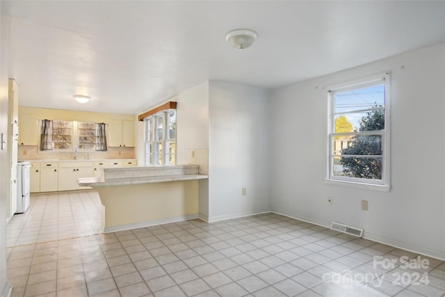 kitchen with sink, white range oven, kitchen peninsula, backsplash, and light tile patterned flooring