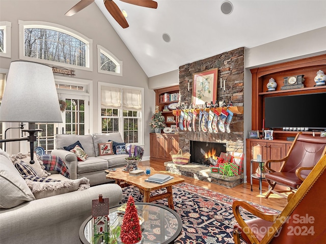 living room featuring a stone fireplace, ceiling fan, high vaulted ceiling, and wood-type flooring