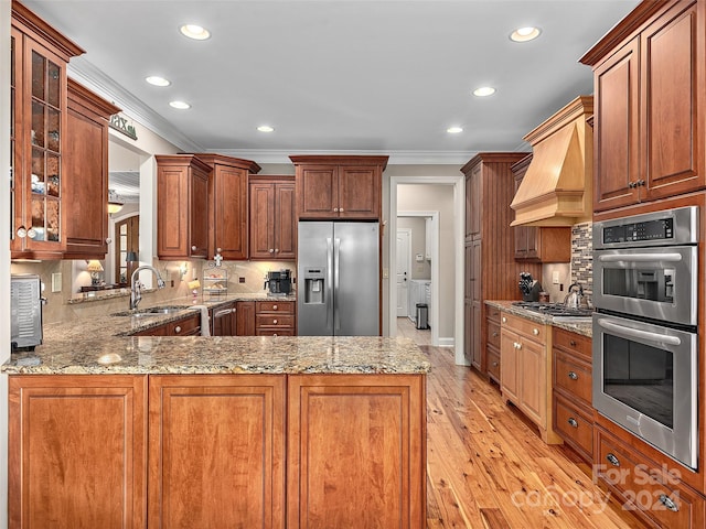 kitchen featuring custom exhaust hood, sink, light hardwood / wood-style floors, kitchen peninsula, and stainless steel appliances