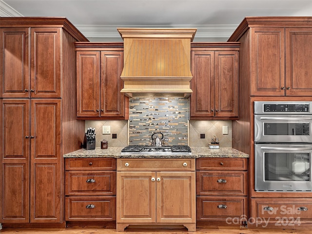 kitchen with appliances with stainless steel finishes, light stone counters, crown molding, and custom exhaust hood