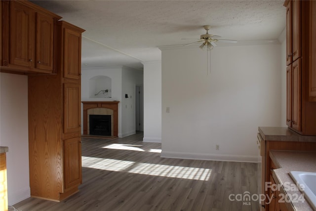 unfurnished living room featuring ceiling fan, light wood-type flooring, a textured ceiling, a tiled fireplace, and ornamental molding