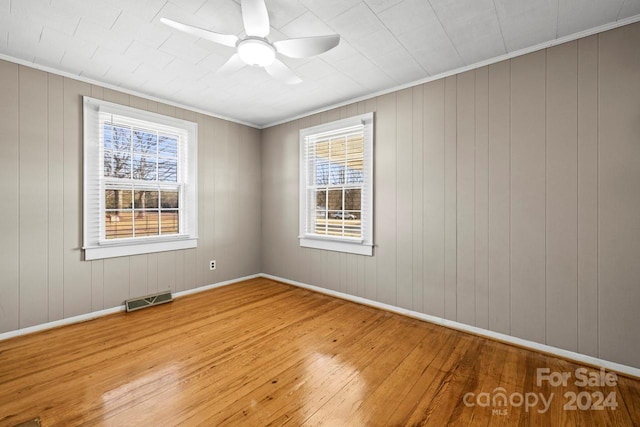 spare room with light hardwood / wood-style flooring, ceiling fan, ornamental molding, and wood walls