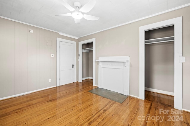 unfurnished bedroom with ceiling fan, hardwood / wood-style floors, crown molding, and two closets