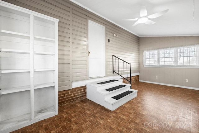 staircase with ceiling fan, wooden walls, vaulted ceiling, and ornamental molding