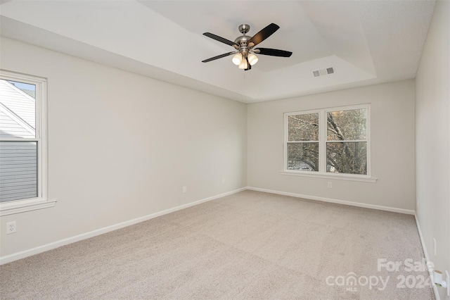 unfurnished room with a raised ceiling, plenty of natural light, ceiling fan, and light colored carpet