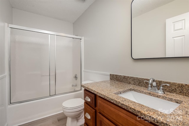 full bathroom with bath / shower combo with glass door, a textured ceiling, toilet, vanity, and hardwood / wood-style flooring