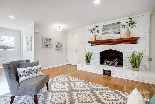 living room featuring light wood-type flooring, a brick fireplace, and ornamental molding