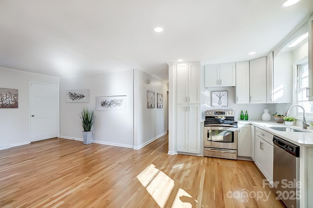 kitchen with appliances with stainless steel finishes, light wood-type flooring, white cabinetry, and sink