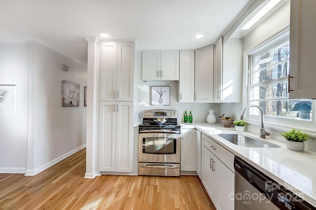 kitchen with light wood-type flooring, ornamental molding, stainless steel appliances, sink, and white cabinetry