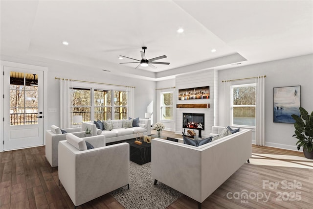 living room with a raised ceiling, ceiling fan, a fireplace, and hardwood / wood-style floors