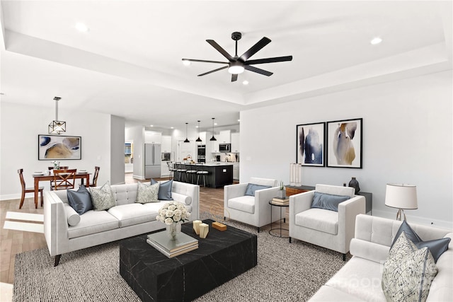 living room with a raised ceiling, ceiling fan, and wood-type flooring