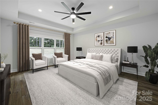 bedroom with ceiling fan, dark hardwood / wood-style floors, and a raised ceiling