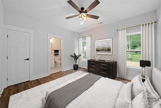 bedroom featuring multiple windows, ceiling fan, ensuite bathroom, and dark hardwood / wood-style floors