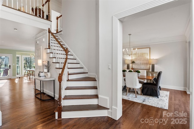 stairs with baseboards, ornamental molding, a chandelier, and wood finished floors